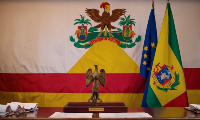 Varios documentos de contrato, leyes y reglamentos sobre una mesa con bandera boliviana en el fondo.
